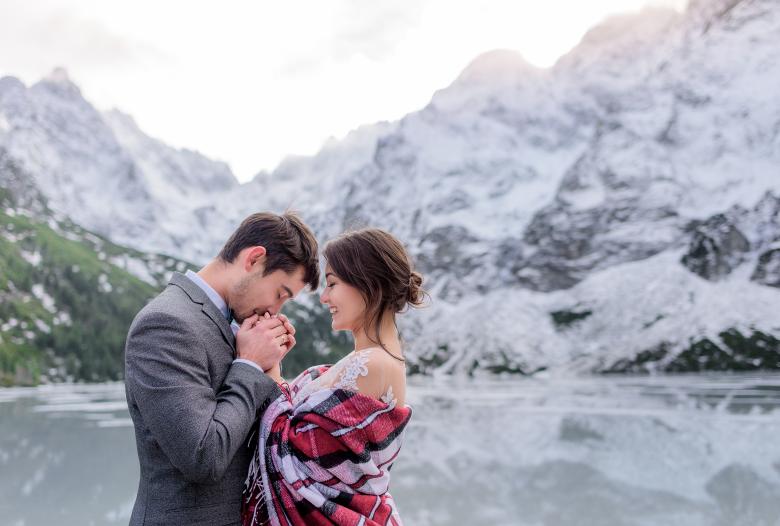 Man kissing woman's hands in front of a frozen lake