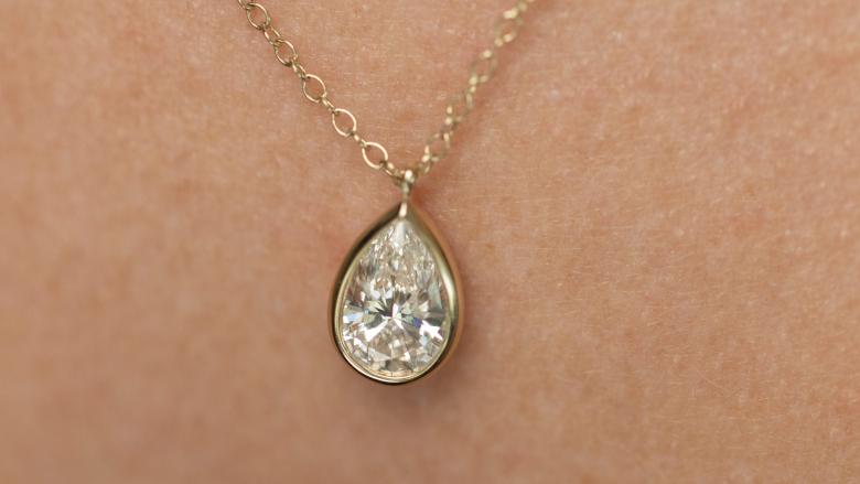 Close up of a tear drop shape solitaire new brilliance pendant being worn by a woman