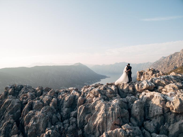 Photo of bride and groom kissing standing together on rocky mountains