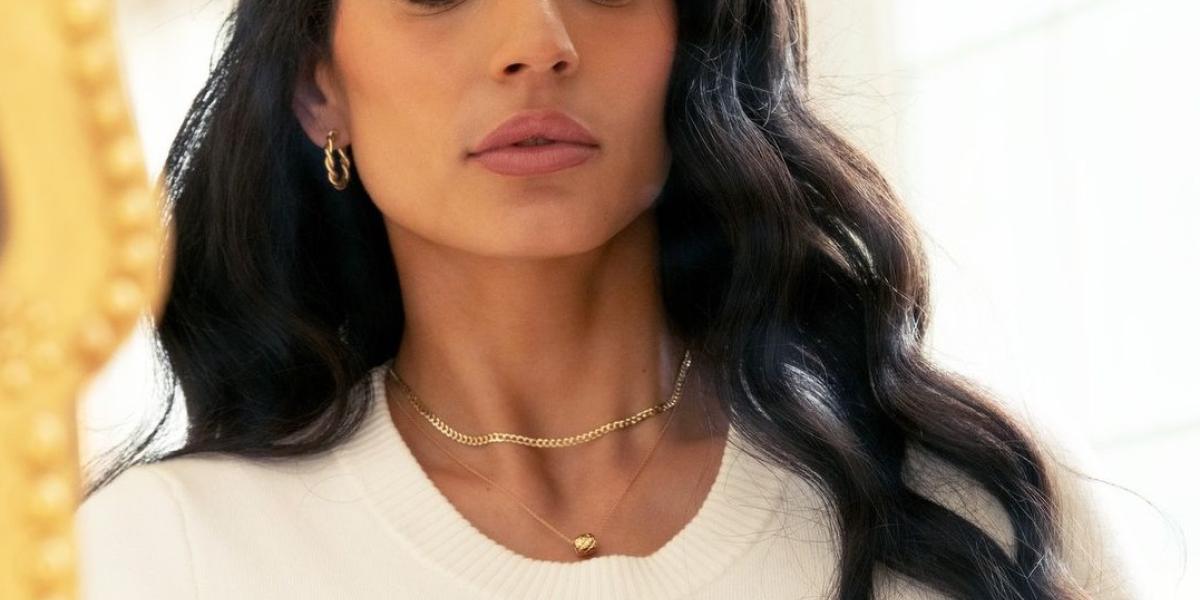 Elegant woman wearing gold jewelry, including rings, necklace, and earrings, gazing into a mirror.