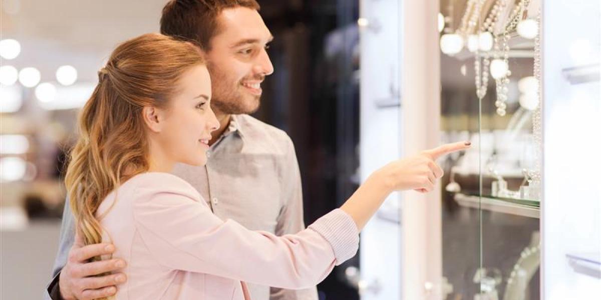 Happy couple browsing jewellery displays in a store, pointing at elegant necklaces and accessories.